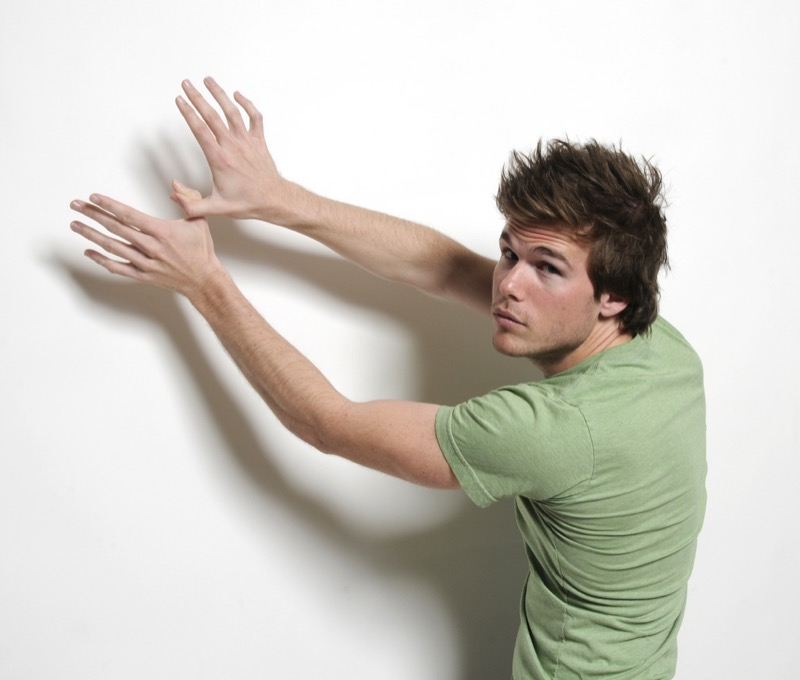 Colin Wright in a green shirt posing against a white wall for an Exile Lifestyle promotional photograph